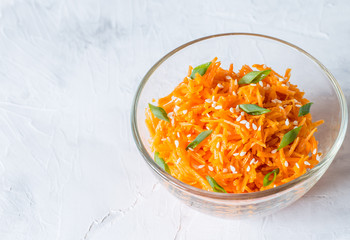 (Asian) Korean carrots-pickled, spicy salad of sliced carrots with spices and garlic in a transparent salad bowl on a light background close-up. A dish of Eastern vegetarian cuisine.