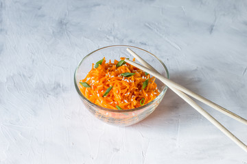 (Asian) Korean carrots-pickled, spicy salad of sliced carrots with spices and garlic in a transparent salad bowl on a light background close-up. A dish of Eastern vegetarian cuisine.