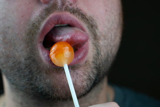 Bearded guy licking candy on a stick imitating oral sex