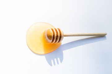 Drops of spilled fresh honey and a wooden ladle on a white background, top view