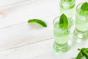 Summer Sweet Refreshing Mint Liqueur Cocktail Shots with Ice and Mint Leaves on White Wooden Background. Selective focus.