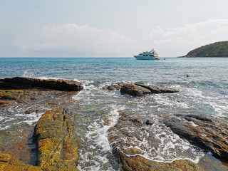 The yacht sails on sea water in the early morning. View from the rocky shore.