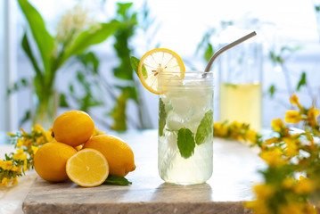 Citrus iced lemonade in pitcher and lemons glasses with lemon slice decoration and on marble table on natural background