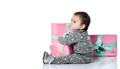 Baby girl in gray suit and boots. She playing with decoration on pink gift box, sitting on floor isolated on white. Close up