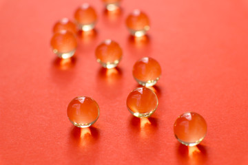 Transparent round capsules of vitamins - Fish oil pills close-up. Small gold-yellow balls on a red background. Concept of treatment and prevention of health. 