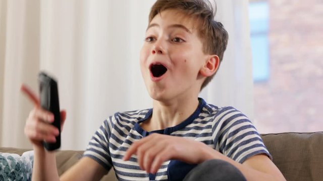 childhood, technology and leisure concept - happy boy with popcorn and remote control watching tv at home