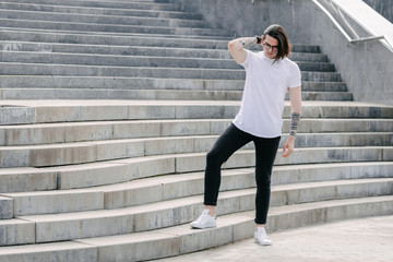 Fototapeta premium Hipster handsome male model wearing white blank t-shirt with space for your logo or design in casual urban style