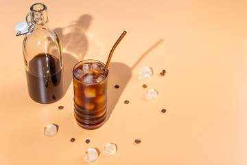 Cold brew coffee with ice cubes in glass and cofee beans on beige background,hard light,top view