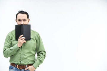 Mature businessman peeking over black notebook with suspicious, distrustful face expression over white background with copyspace for text or product.