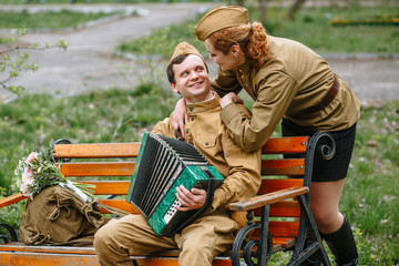 People in Soviet military uniforms. A soldier is sitting on a bench, playing an accordion. Behind...