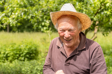 Portrait of smiling Elderly man wearing a hat in the his garden in springtime.