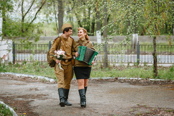 People in Soviet military uniforms. A soldier walks down the alley, hugging a military girl playing...