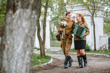 People in Soviet military uniforms. A soldier walks down the alley, hugging a military girl playing...
