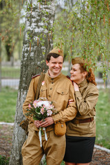 People in Soviet military uniforms. A couple stands by a tree
