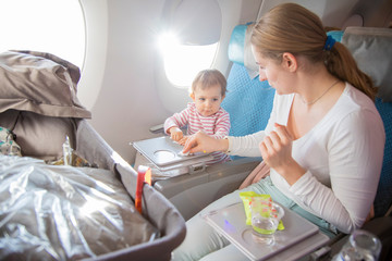 a little cute toddler girl sitting in an airplane in a chair at the porthole wipes with her mother a folding table with a wet antibacterial wipe before eating.