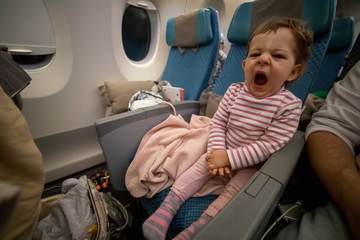 Fototapeta premium little cute sleepy baby is sitting in an airplane chair and yawning after a comfortable sleep on a long flight
