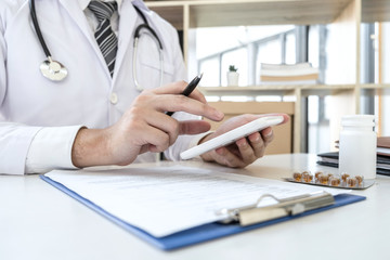 Doctor working with digital tablet in clinic and medical stethoscope, medicine on clipboard on desk