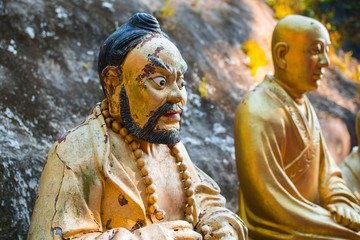 Beautiful buddha statue unique close shot. Golden sculpture representing an angry buddhist/monk. Main path/alley, Ten Thousand Buddhas Monastery, Sha Tin, Hong Kong. Peaceful sunlight.