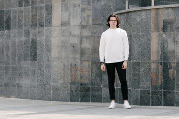 Man wearing white sweatshirt or hoodie and glasses outside on the city streets. Sweatshirt or hoodie for mock up, logo designs or design prints with free space