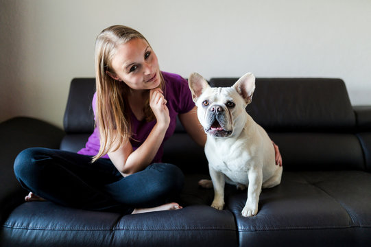 Woman is sitting with french bulldog on couch