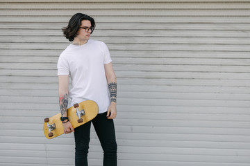 Hipster handsome male model wearing white blank t-shirt with space for your logo or design in casual urban style. He is holding a skateboard © 4Max