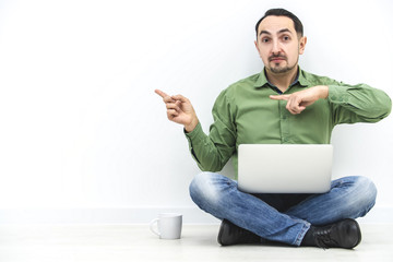 Presentation concept. Smart businessman holding laptop and pointing to copy space for key words against white wall background.