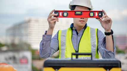 Asian maintenance worker man holding red aluminium spirit level tool or bubble levels over tool box at construction site. Equipment for civil engineering project