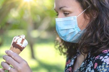 Summertime and virus. Beautiful girl wearing a face mask looking down at an ice cream in her hand.