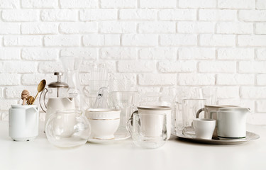 ceramic and glass cups and tableware on the table on white brick wall background