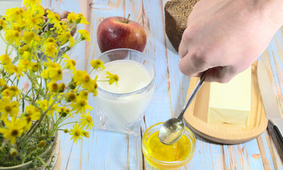 A male hand holds a spoon with honey. A man prepares breakfast, made from natural products. Butter and bread for a sandwich, on the table.