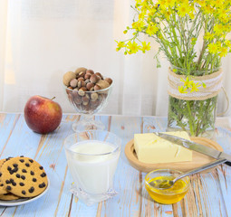 Homemade natural products for the child for breakfast. A bouquet of yellow wildflowers in a vase. Cookies with milk on the table.