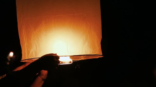 People launching a Chinese sky fly fire lantern in the night sky to make a wish during festival.