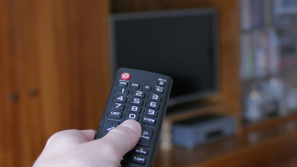 Hand with tv remote control switching television on at home