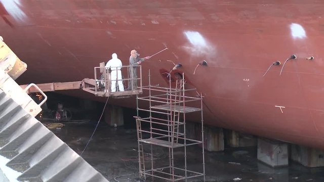 worker painting ship in shipyard drydock