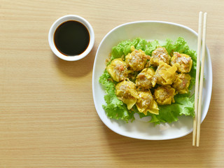 Dumpling arranged on a plate with a sauce for dunking on a wooden table.
Shu Mai served on a plate on a wooden background.
