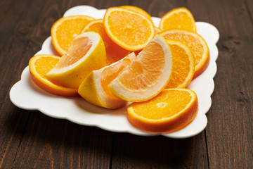 Naklejka na ściany i meble Fresh orange fruits sliced on a plate, dark wooden background - natural and healthy food.