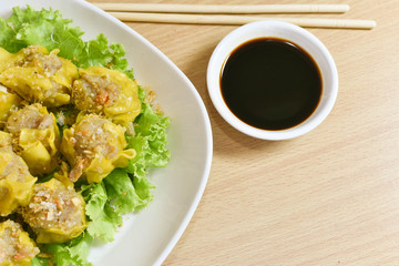 Dumpling arranged on a plate with a sauce for dunking on a wooden table.
Shu Mai served on a plate on a wooden background.