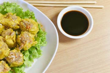 Dumpling arranged on a plate with a sauce for dunking on a wooden table.
Shu Mai served on a plate on a wooden background.