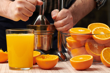 Squeezing an orange with a manual press, close view, making a glass of fresh. Fresh oranges on a wooden table, whole, squeezed and sliced.