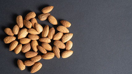 A handful of almond on black background. Portion of almond nuts. Closeup peeled almonds. Top view with copy space.