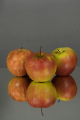 Three red apples on mirroring table on mirror gray background with reflection isolated close up