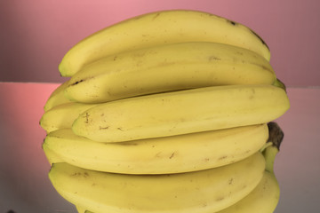 Naklejka na ściany i meble A bunch of bananas on mirroring table on mirror red background with reflection isolated close up