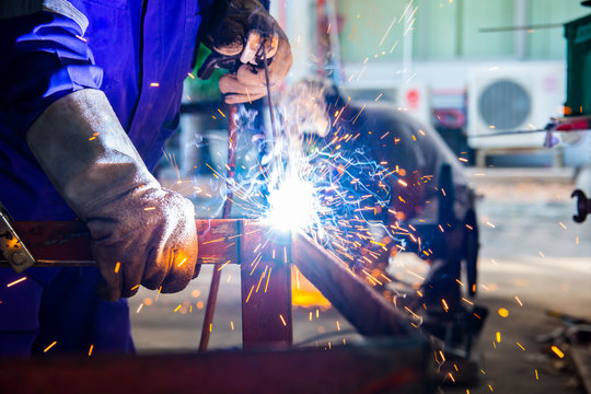 Welder in blue uniform welding the workpiece.