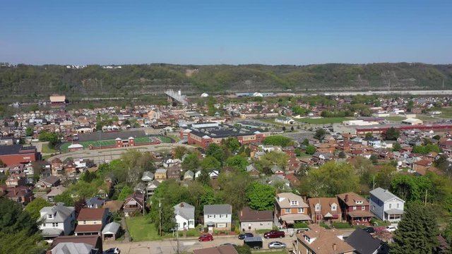 A summer cinematic orbiting aerial establishing shot of a small Pennsylvania town. The Ohio River in the distance. Pittsburgh suburbs. Flown with FAA authorization.  	