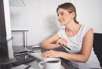 Beautiful happy woman holding credit card in hand and using laptop computer keyboard. Businesswoman or entrepreneur working. Online shopping, e-commerce, internet banking, spending money concept