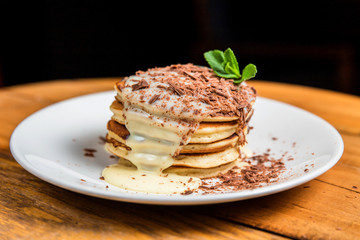 A stack of pancakes with condensed milk, chocolate crumbs and mint on a white plate