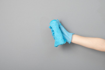 A female hand in a rubber glove holds a microfiber rag on a gray background