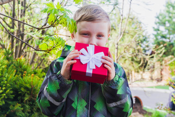 Baby boy blond European received a gift in a red box in the spring in nature for his birthday.
