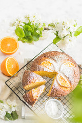 Round cupcake with orange with icing sugar on a wire rack with a cut piece of cake with flowers on a gray background vertical arrangement