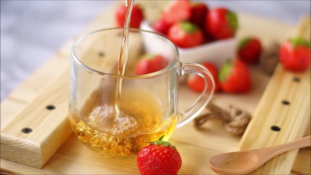 hot black tea with strawberry berries, poured into a transparent mug. on a wooden Board